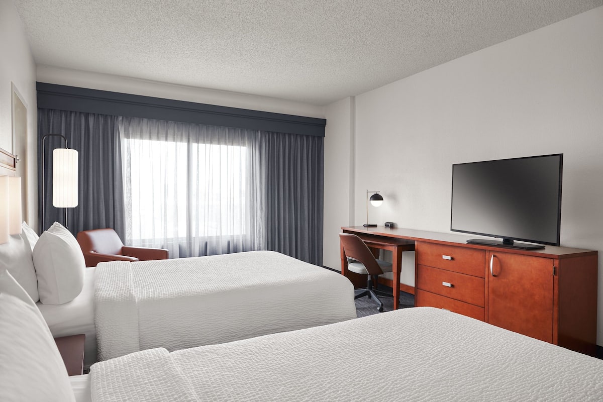 Une chambre d’hôtel avec deux lits, un bureau, une télévision et une chaise.