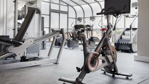 A gym with exercise equipment, including a treadmill and an elliptical machine, under a large glass ceiling.