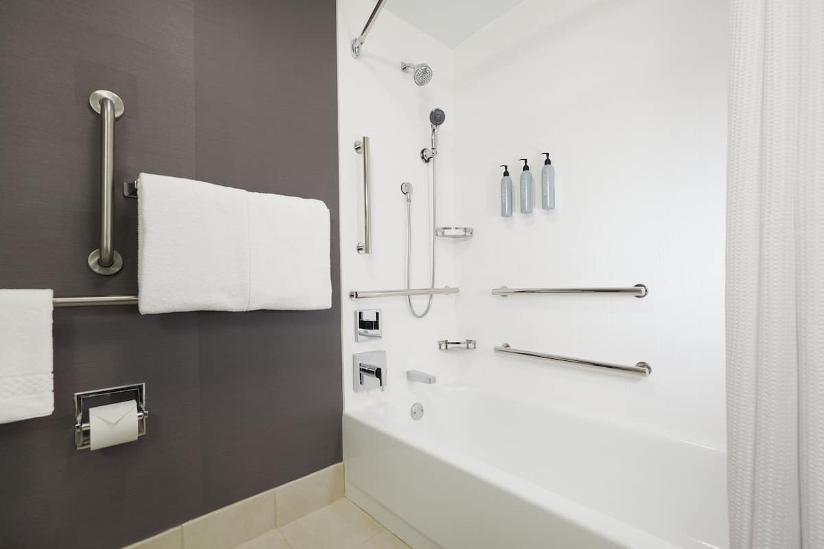 Une salle de bain moderne équipée d’une baignoire, d’une douche et de barres d’appui.