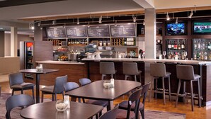 A modern bar area with multiple seating options, a counter with a menu, and a television screen displaying sports.