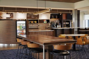 Un espace bar moderne doté d’un long comptoir, de tabourets et d’un réfrigérateur rempli de boissons.