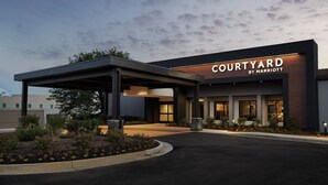 A modern hotel entrance with a covered walkway, a landscaped garden, and a clear sky.
