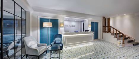 Zona de recepción de un hotel con mostrador, dos sillones, una escalera y baldosas de suelo con diseño.