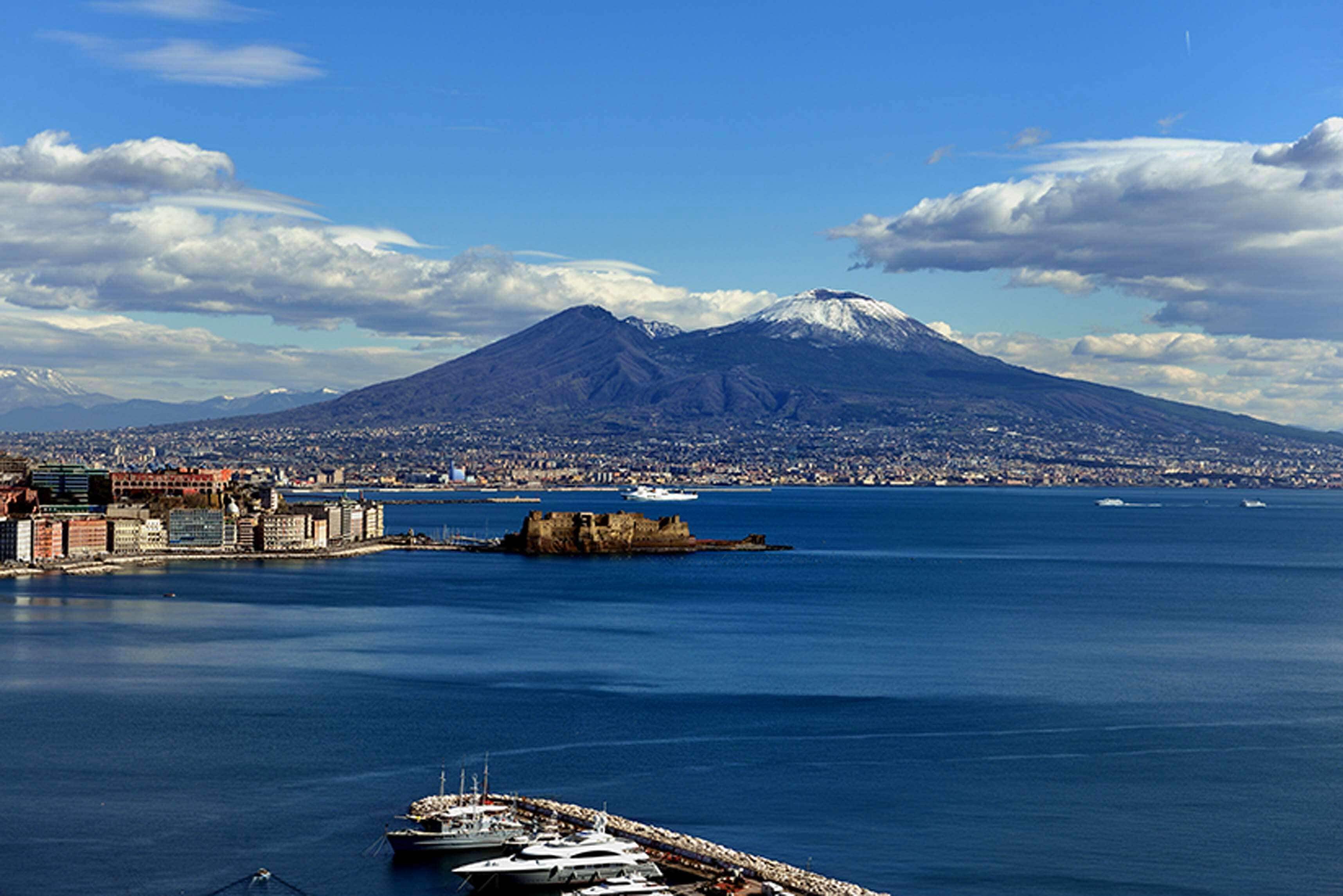 A coastal city with a prominent mountain in the background, a marina with boats, and a historic fort.