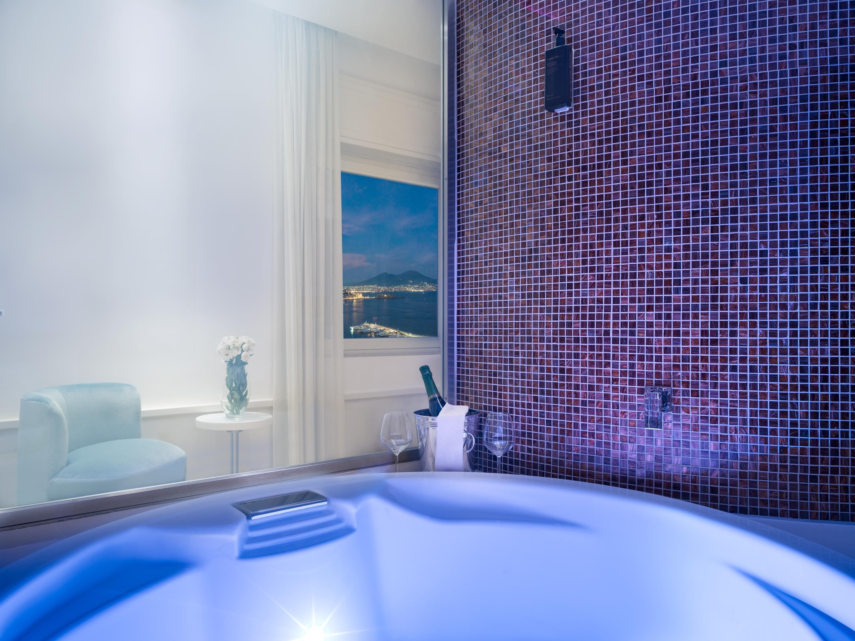A modern bathroom with a bathtub, a glass partition, and a view of a cityscape at night.