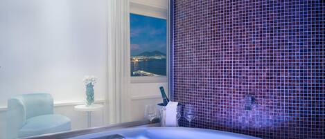 A modern bathroom with a bathtub, a glass partition, and a view of a cityscape at night.