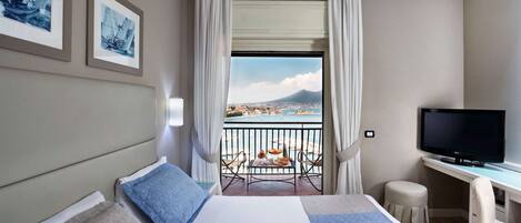 A hotel room with a bed, a desk, a TV, and a balcony with a view of a city and a mountain.
