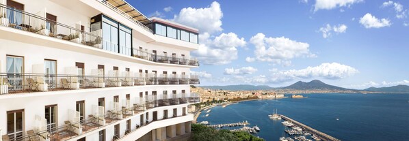 A multi-story hotel with balconies overlooking a marina and a coastal cityscape.