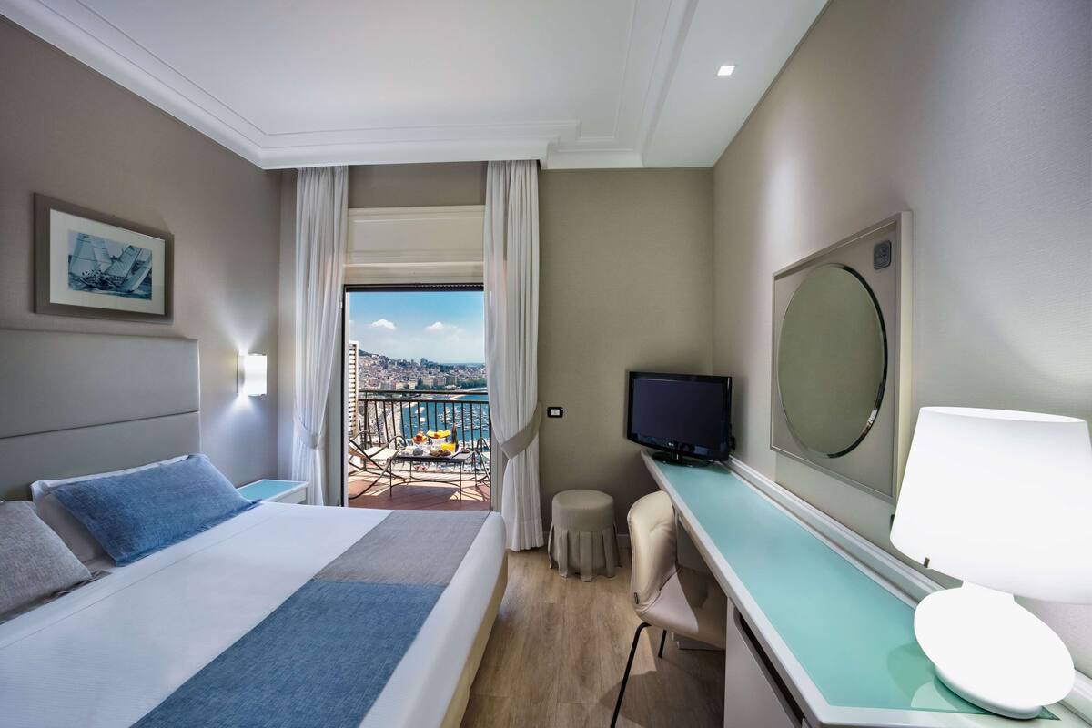 A hotel room with a bed, a desk, a television, and a view of a cityscape.