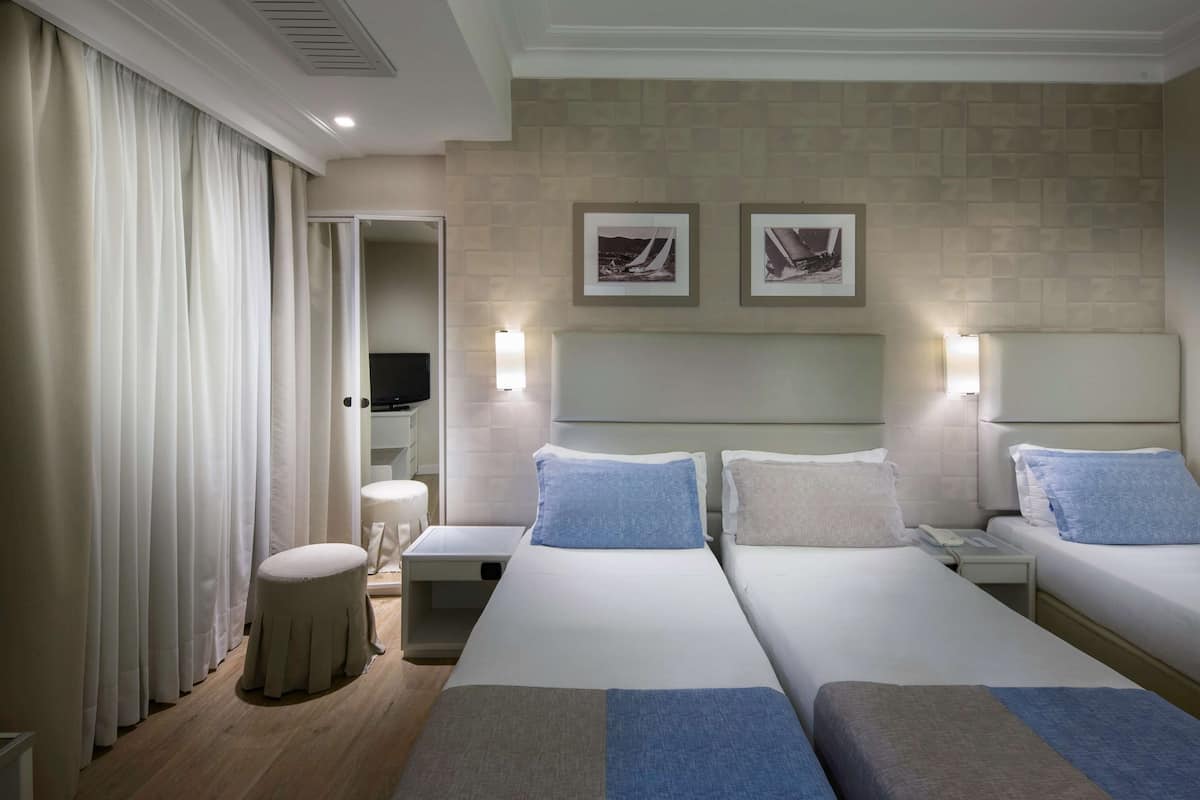 A hotel room with two beds, a small stool, a nightstand, and a TV.