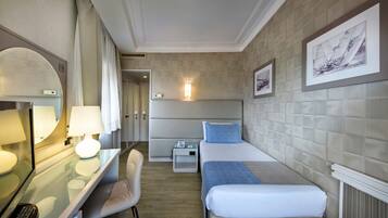 A hotel room with a bed, bedside table, lamp, chair, and a desk with a computer.