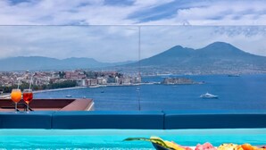 A balcony with a pool, a fruit bowl, and a view of a cityscape with a mountain in the background. - Hotel Paradiso, BW Signature Collection (Naples)