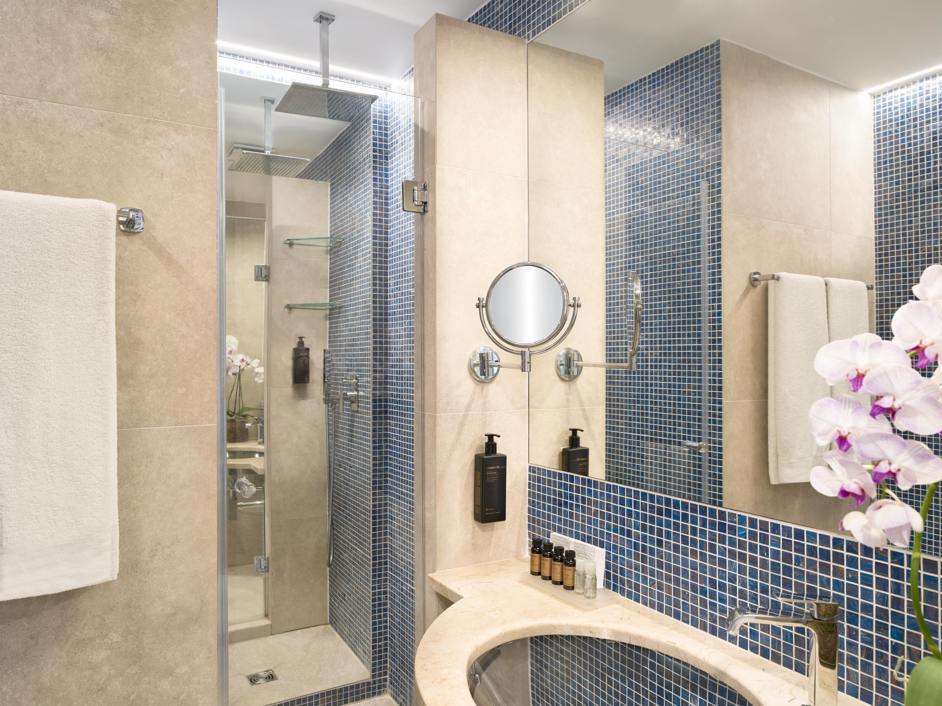 Casa de banho moderna com cabine de duche em vidro, lavatório bege com espelho e paredes revestidas a azulejos azuis.