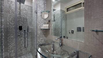 Een moderne badkamer met een douchecabine van glas, een glazen wastafel en betegelde wanden.