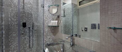 Un baño moderno con cabina de ducha de vidrio, lavamanos de cristal y paredes con azulejos.
