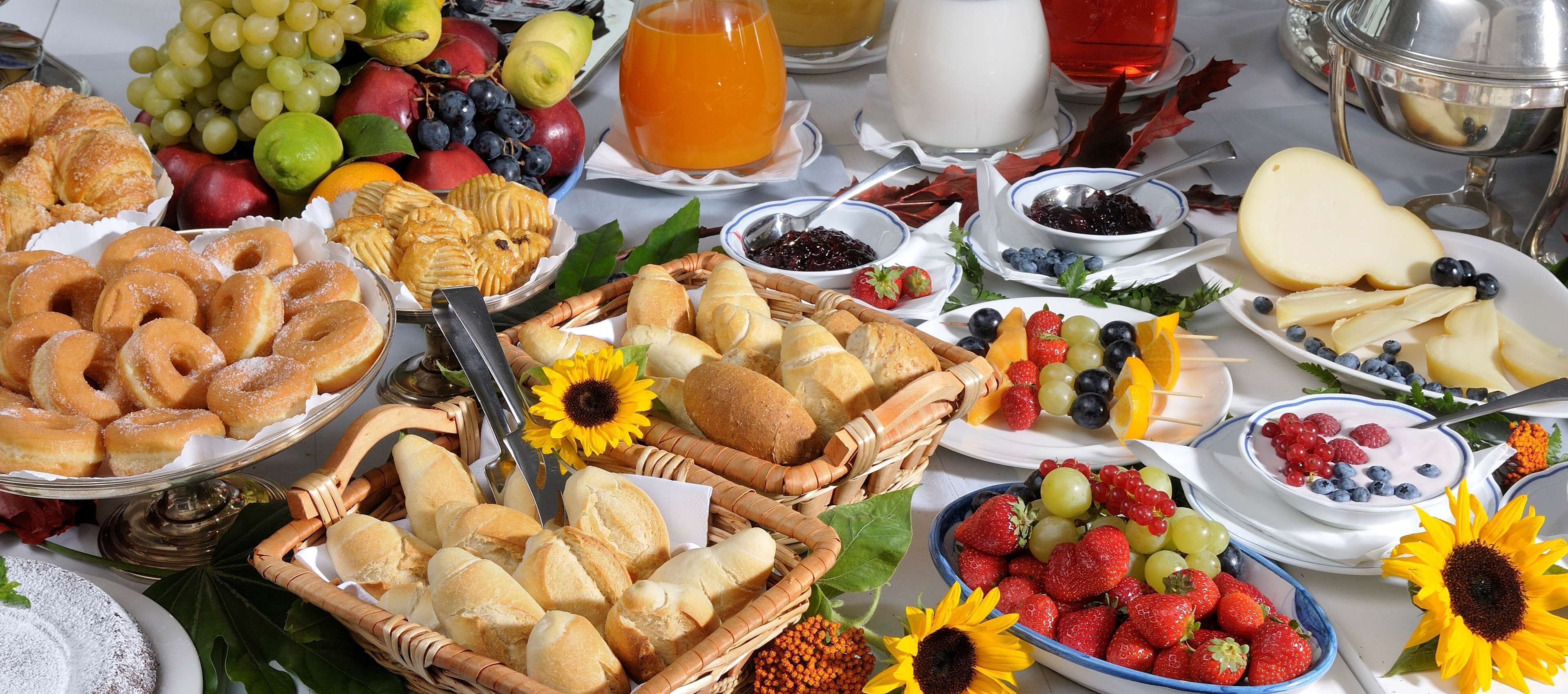 Una mesa llena de diversas comidas, entre ellas pasteles, pan, frutas y queso.