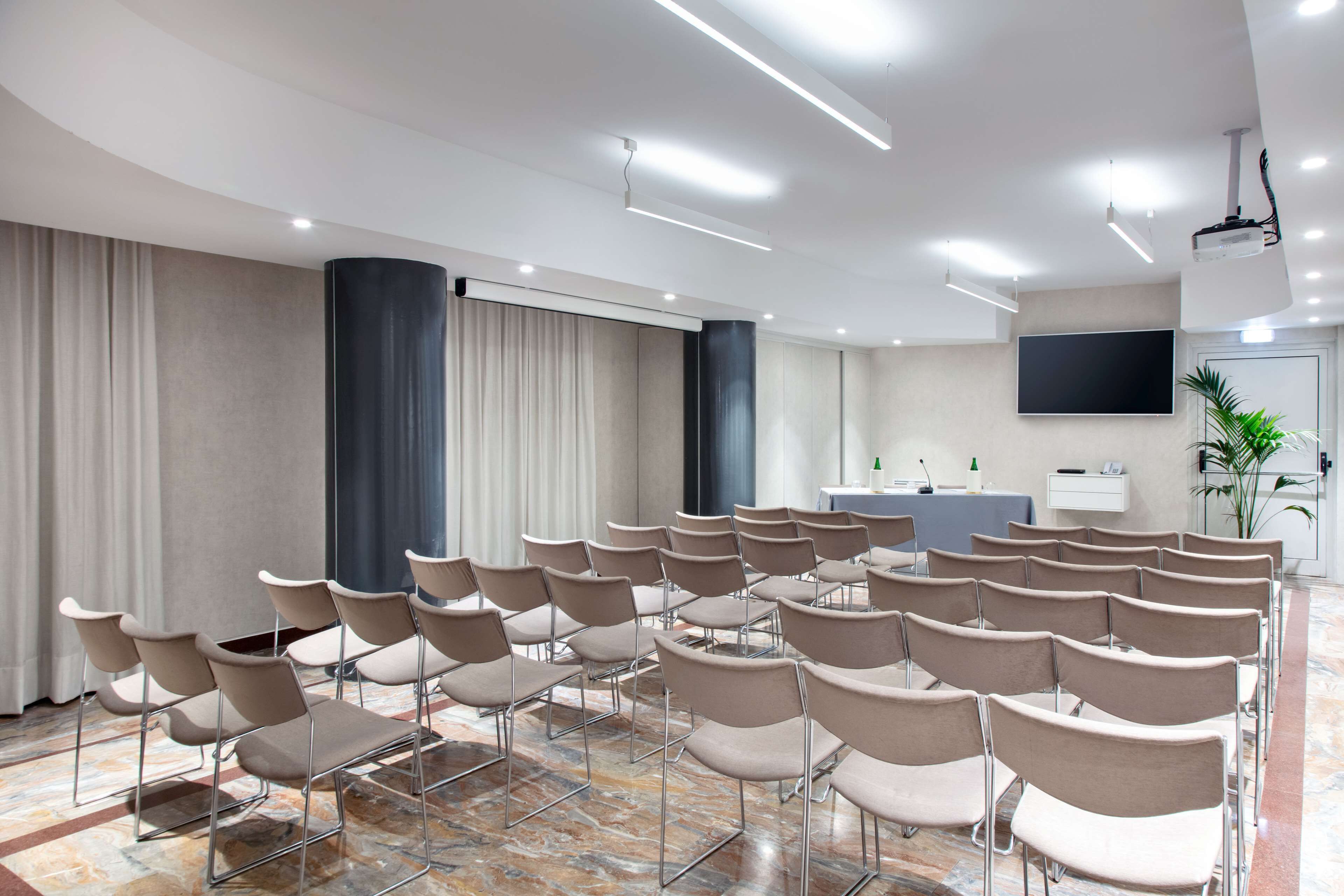 Een congrescentrum met rijen stoelen, een spreekgestoelte, een flatscreen televisie en een receptiebalie.