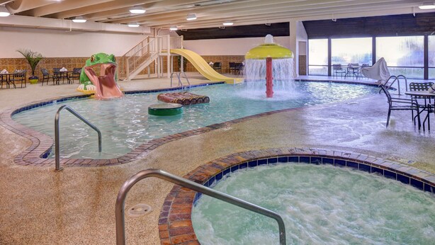 An indoor swimming pool with a slide, a water feature, and seating areas. - Best Western Plus Midwest Inn (Omaha)