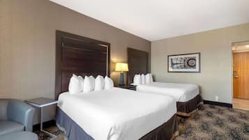A hotel room with two beds, a desk, a chair, a lamp, and a wall art piece.