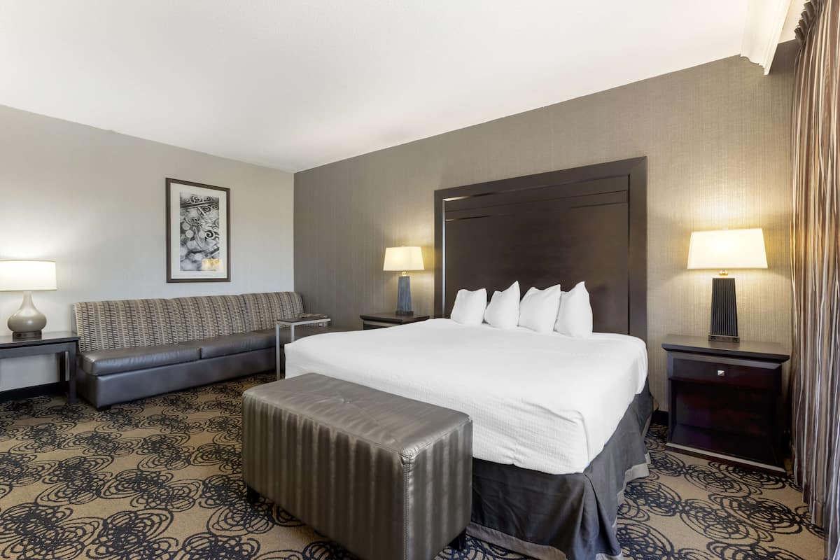 Quarto de hotel com uma cama grande, um sofá, uma mesa pequena e um abajur.