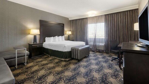 A hotel room with a large bed, a desk, a chair, a small table, and a TV. - Best Western Plus Midwest Inn (Omaha)