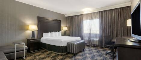 A hotel room with a large bed, a desk, a chair, a small table, and a TV.
