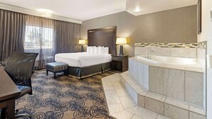 A hotel room with a bed, a desk, a chair, a bathroom with a bathtub, and a window with curtains. - Best Western Plus Midwest Inn (Omaha)