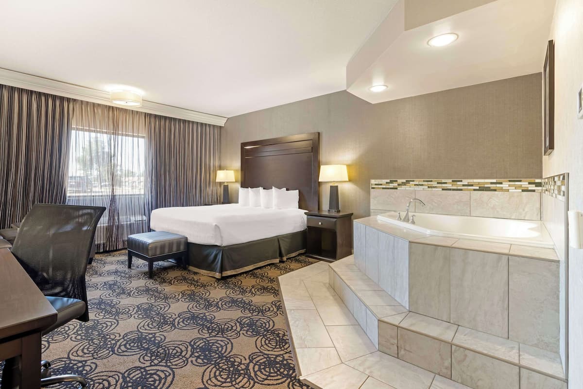 Quarto de hotel com cama, escrivaninha, cadeira, banheiro com banheira e janela com cortinas.