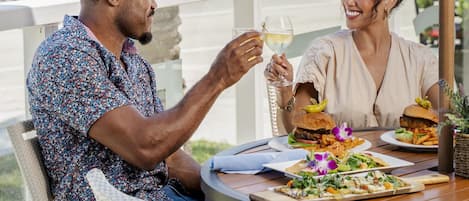 Una pareja cenando al aire libre con vista a palmeras y al océano.
