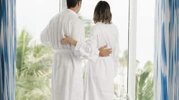 Una pareja vestida de blanco de pie junto a una ventana con vistas a palmeras.