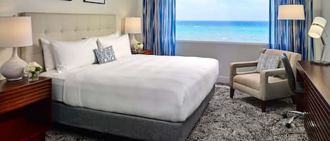 Habitación de hotel con una cama grande, una silla, un escritorio y vistas al océano.
