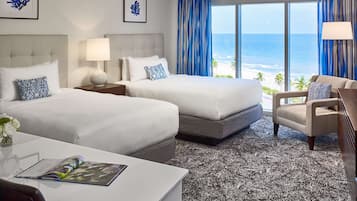 Habitación de hotel con dos camas, un escritorio, una silla y vista al océano.