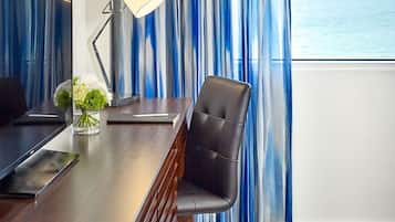 A hotel room with a wooden desk, a black leather chair, a lamp, and a vase with flowers.
