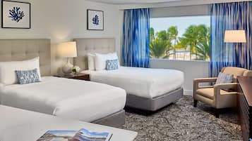 Quarto de hotel com duas camas, uma cadeira, uma mesa, um abajur e vista para palmeiras.