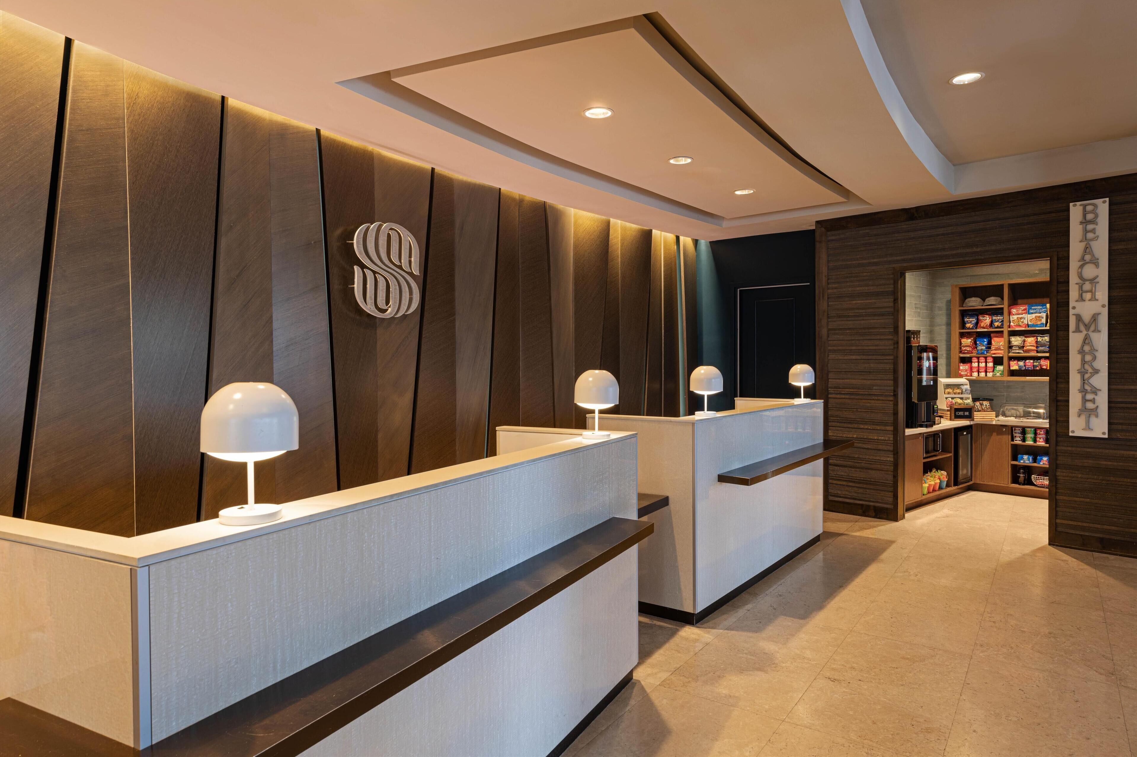 Un espace d’accueil au design moderne, comprenant un mur revêtu de panneaux en bois, un logo et un comptoir agrémenté d’une lampe.