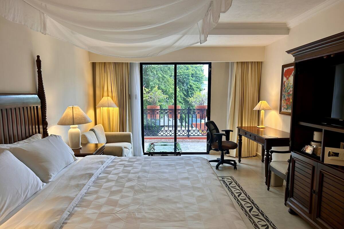 Una habitación de hotel con una cama grande, un escritorio con silla, televisión y un balcón con cortinas.
