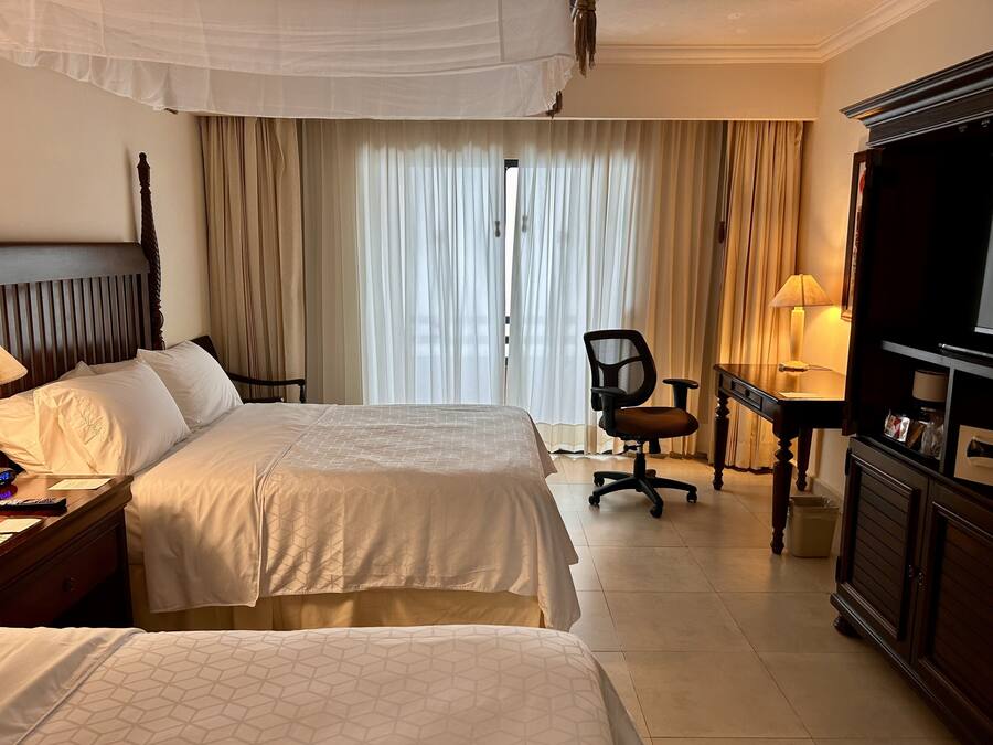 Una habitación de hotel con dos camas, un escritorio, una silla, un televisor y cortinas.