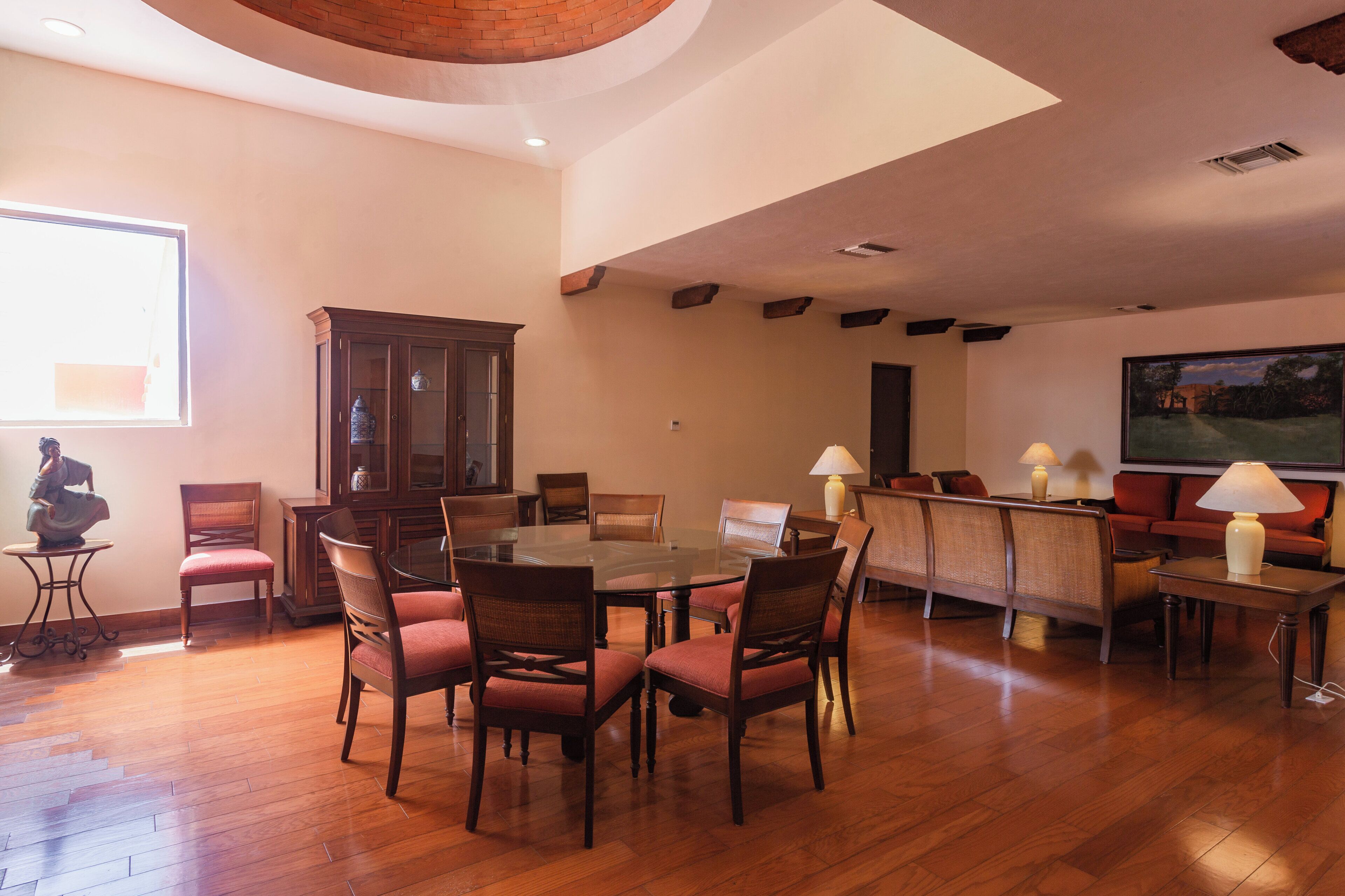 Uma sala de estar ampla com piso de madeira, uma grande mesa de jantar rodeada por cadeiras, um conjunto de sofás e um armário.