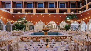 Un vestíbulo de hotel con varias mesas de comedor, una fuente central y balcones con barandillas.