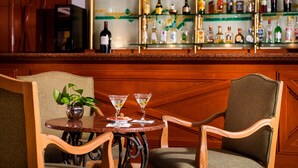 Una zona de bar con una mesa redonda, dos sillas, una planta en maceta y una vitrina llena de botellas.