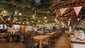 Un espacio de comedor al aire libre con mesas y sillas, luces colgantes y techo de madera rústica.