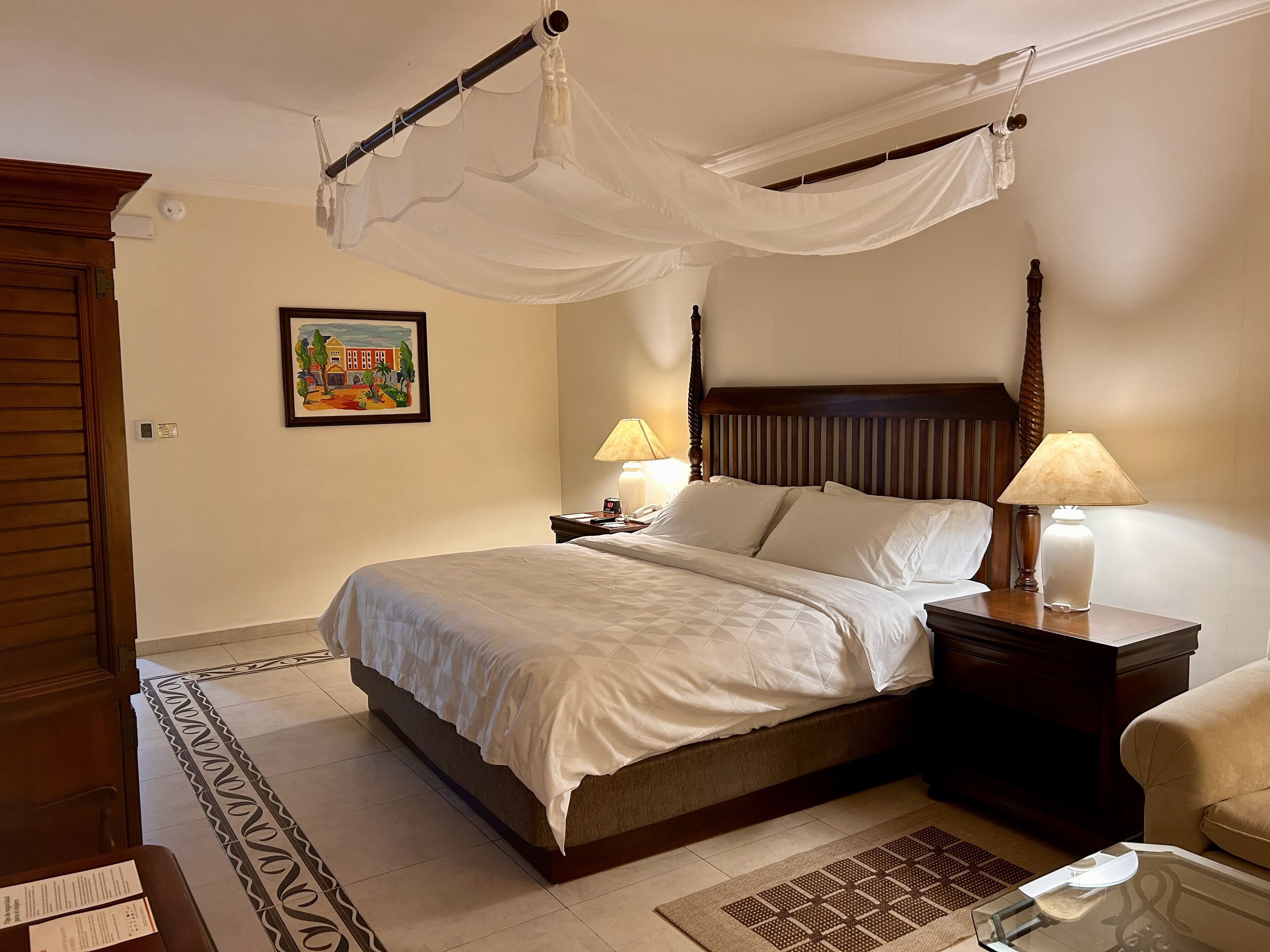 A neatly arranged bedroom with a bed, bedside lamps, a nightstand, a chair, and a decorative rug.