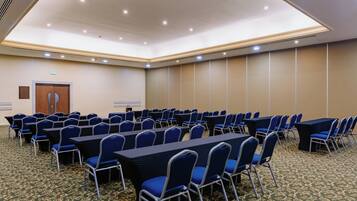 Un salón de conferencias con filas de mesas y sillas, una puerta y suelo alfombrado.