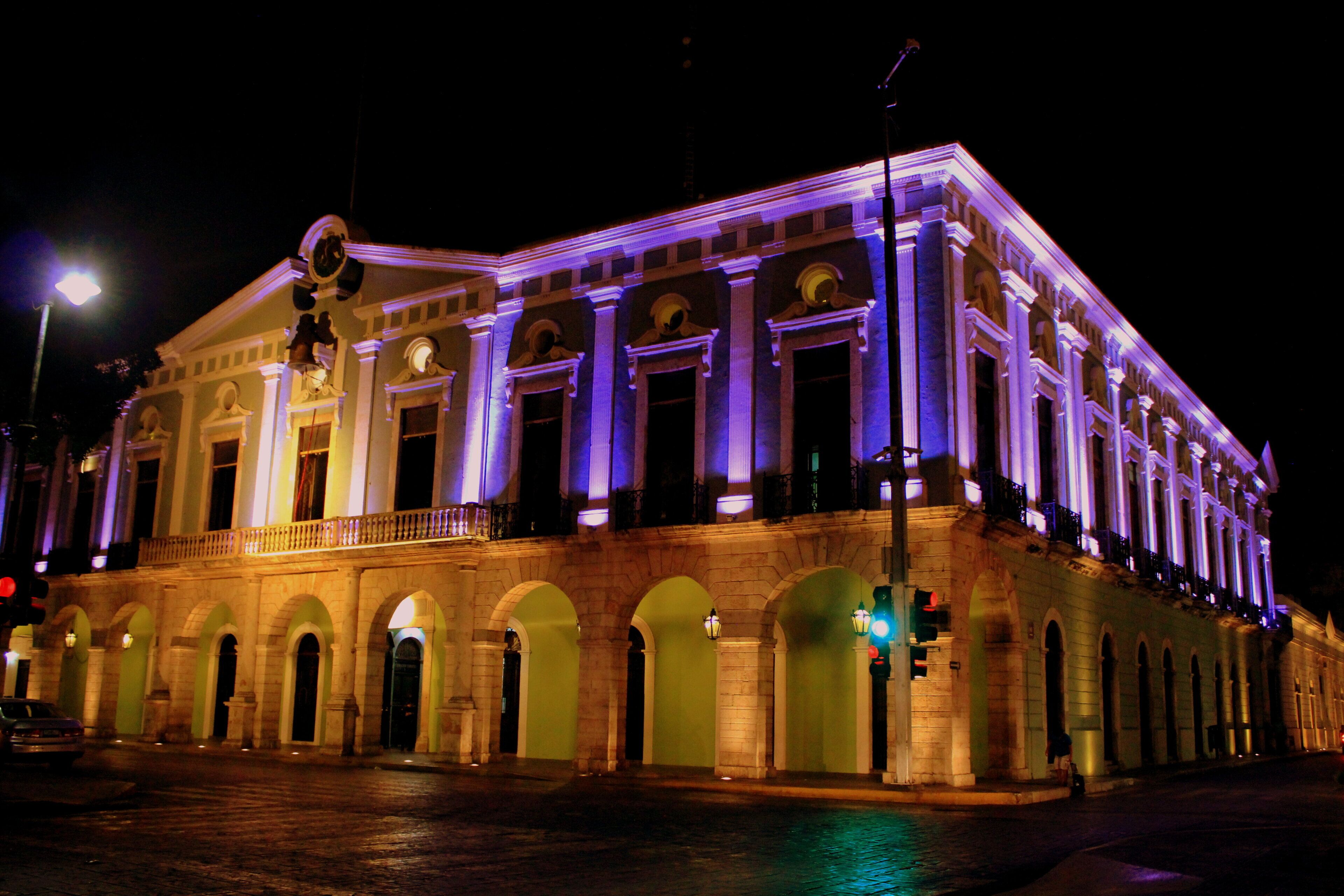A historic building with classical architecture, featuring a central entrance with columns, arched doorways, and a balcony with railings.