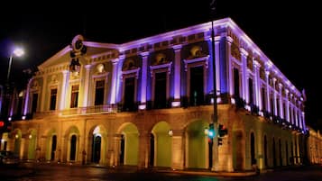 A historic building with classical architecture, featuring a central entrance with columns, arched doorways, and a balcony with railings.