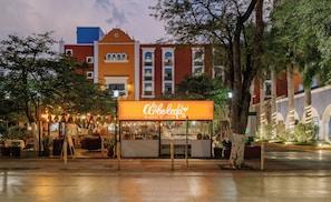 Un restaurante llamado "La Arboleda Bistro & Grill" con terraza y vistas a un edificio rojo con detalles blancos y varias ventanas.