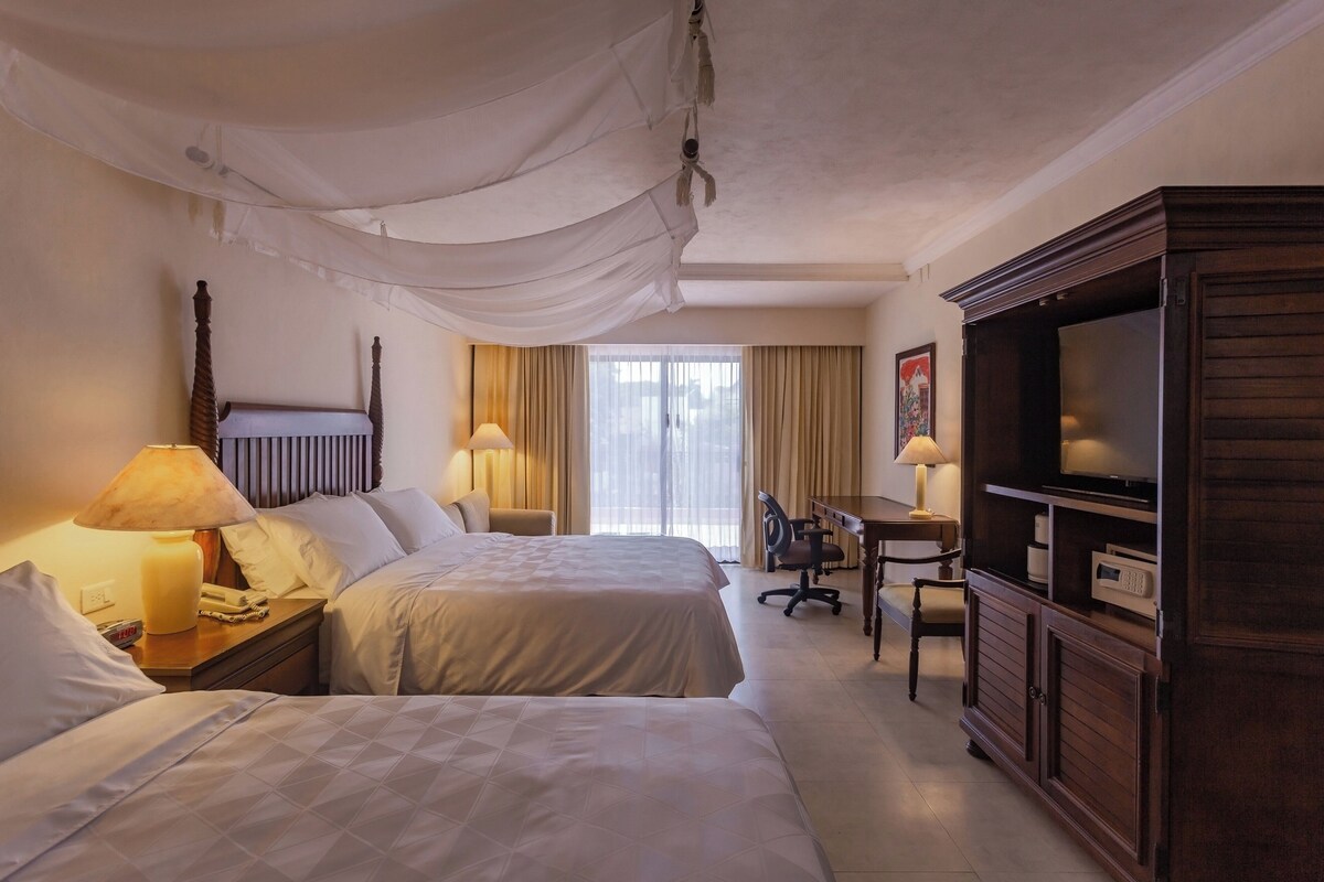 A hotel room with two beds, a desk with a chair, a television, and a cabinet.