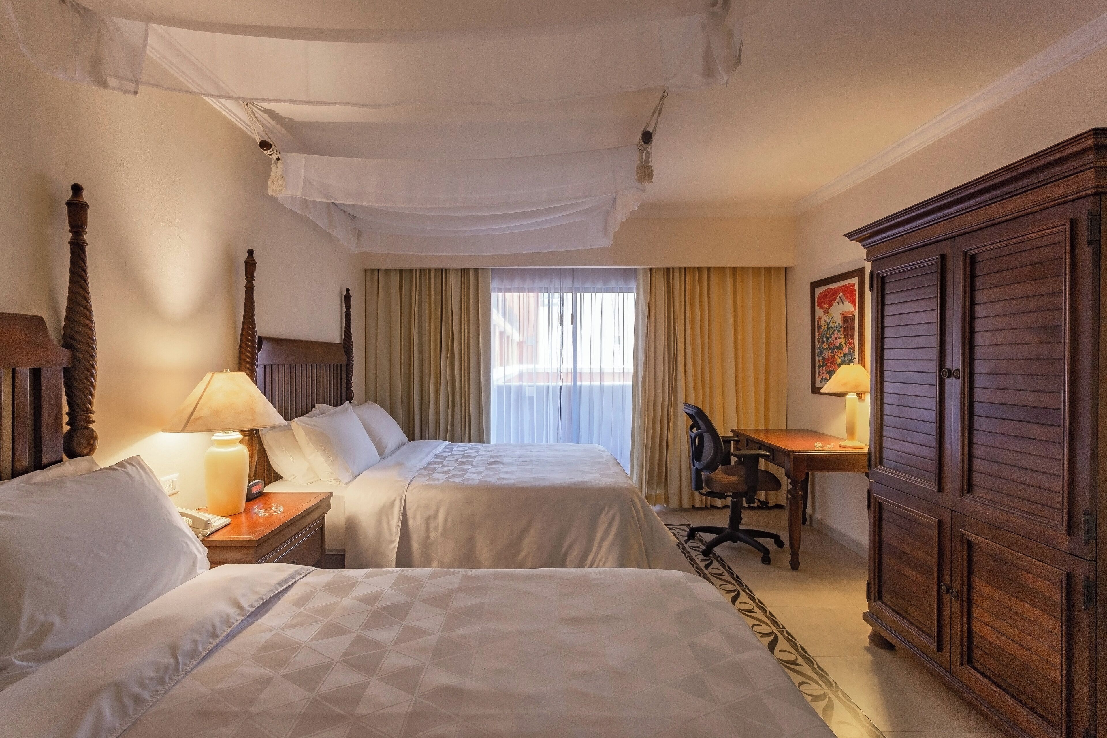 A hotel room with two beds, a desk, a chair, and a wardrobe.