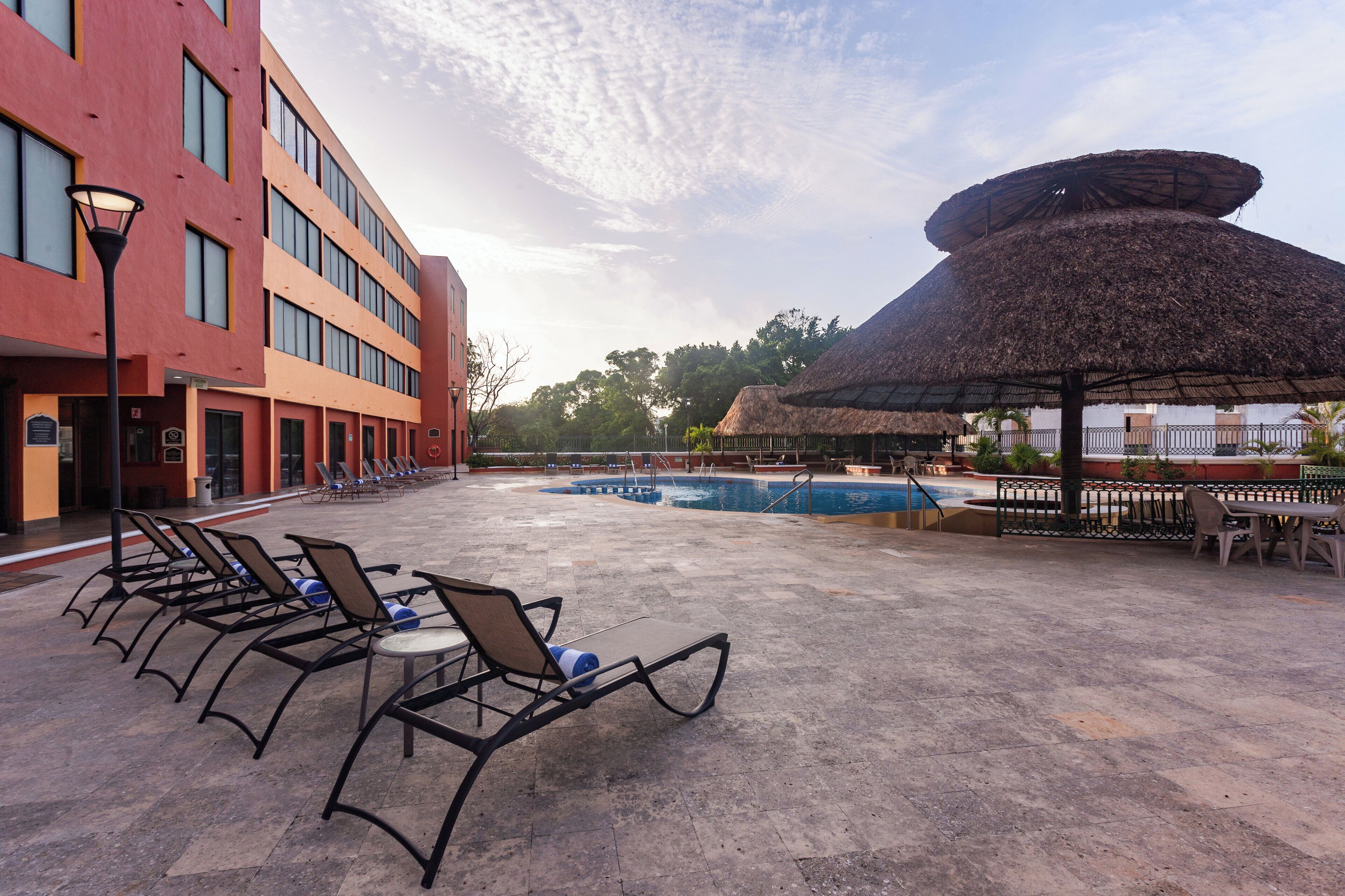 A poolside area with lounge chairs and a thatched umbrella.