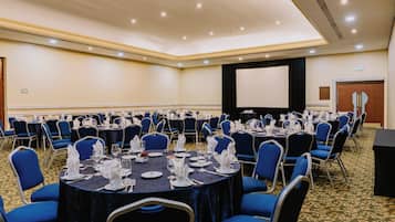 A conference room with round tables set for a meeting, equipped with chairs and tables, a projector screen, and a stage area.